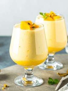 Cocktail smoothie mangue passion servi dans un verre à cocktail avec des petits morceaux de mangue en décoration