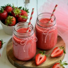 Deux verres type mason jar remplis de smoothie à la fraise, posés sur un dessous de plat en bois.