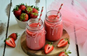 Deux verres type mason jar remplis de smoothie à la fraise, posés sur un dessous de plat en bois.