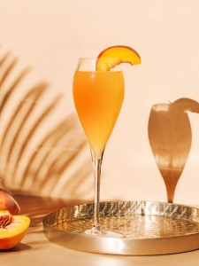 Cocktail Bellini au Prosecco et à la purée de pêche, servi dans un verre à pied décoré d'une tranche de pêche.
