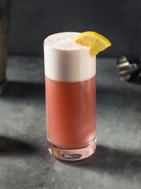 Le Chicago Fizz, un cocktail rose très mousseux, présenté dans un grand verre.