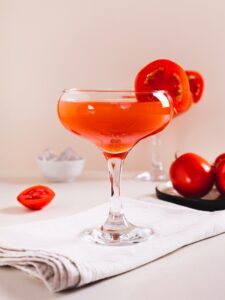 cocktail Tomatini de couleur rouge vif servi dans un verre martini avec une rondelle de tomate sur le bord du verre