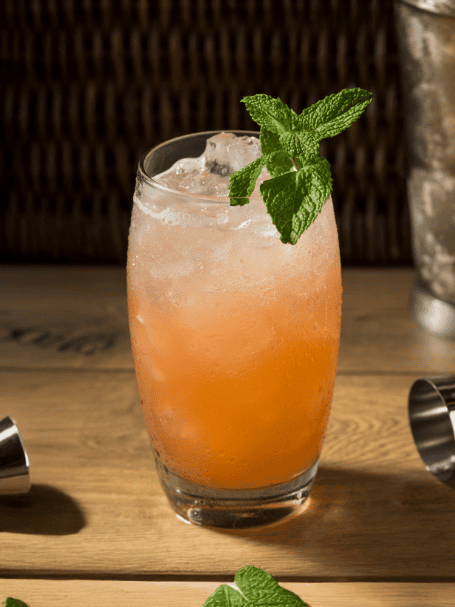 Cocktail virgin planteur, à base de jus d'orange et jus d'ananas et sirop saveur rhum, sans alcool, servi dans un verre avec des glaçons et décoré avec une feuille de menthe