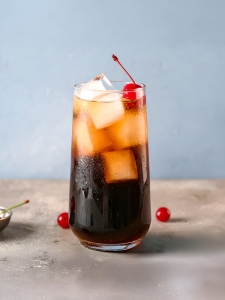 Cocktail sans alcool Roy Rogers, dans un verre long drink rempli de glaçons et décoré d'une cerise confite.