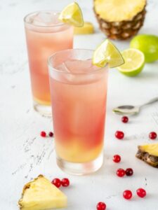 Cocktail Bay Breeze, à base de vodka, jus d'ananas et jus de cranberry. Le cocktail est présenté dans un verre long drink rempli de glaçons, et décoré d'un quartier de citron vert.