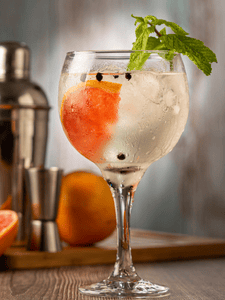 Cocktail gin tonic :avec une rondelle de pamplemousse et des baies de genièvre, servi dans un verre piscine avec des feuilles de menthe en décoration