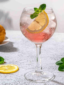 Cocktail avec du gin pink, du tonic, servi dans un verre décoré avec des zestes de citron jaune et des glaçons.