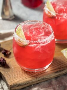 Deux margaritas à l'hibiscus, servis dans des verres shorts drink, givrés de sel et décorés d'un quartier de citron vert.
