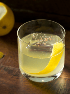 cocktail milk punch clarifié servi dans un verre avec un glaçon et un zeste de citron jaune