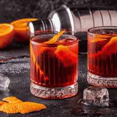Cocktails negroni servi dans un verre old fashioned rafraichi avec des glaçons et décoré avec des zeste d'orange.