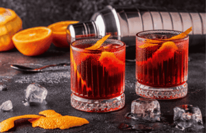 Cocktails negroni servi dans un verre old fashioned rafraichi avec des glaçons et décoré avec des zeste d'orange.