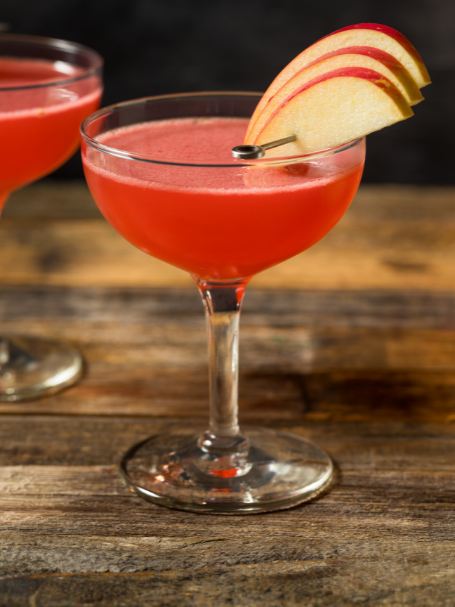 Cocktail Jack Rose, à base de Calvados, jus de citron et grenadine, présenté dans un verre à cocktail décoré de tranches de pomme.