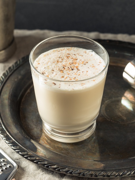 Cocktail Milk Punch, présenté dans un verre short drink et saupoudré de muscade. Une recette à base de rhum ambré, cognac, lait et sucre.