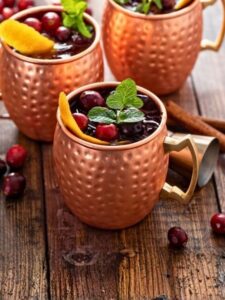 Cocktail Cranberry Moscow Mule dans un verre à mule, à base de vodka, de sirop de canneberge, de ginger beer, de sirop de canne et de citron vert.