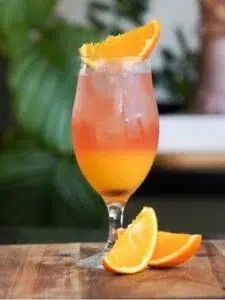 cocktail sex on the beach avec vodka, liqueur de pêche, jus d’orange et jus de cranberry, servi dans un verre décoré avec un quartier d'orange