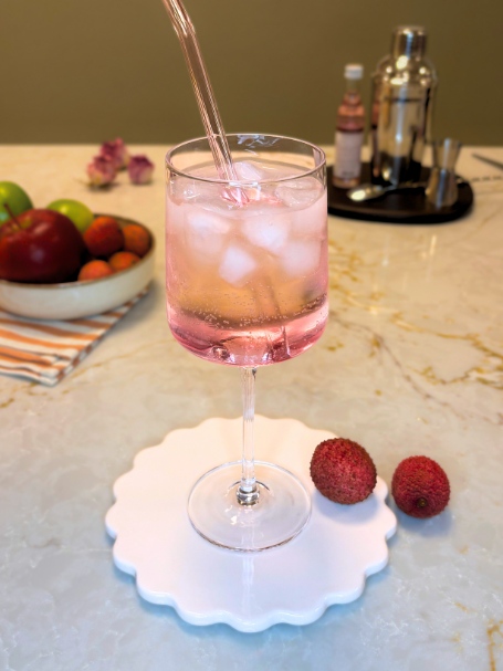 Spritz Litchi, servi dans un verre à vin, avec une paille rose en verre.