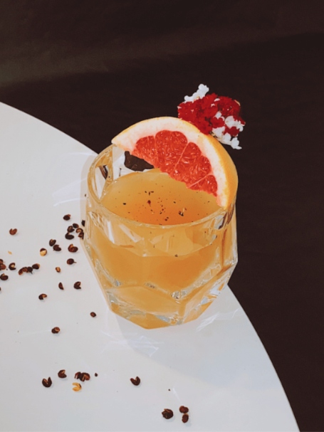 Cocktail sans alcool Tangy Whirl, à base de vin pétillant sans alcool Jaillance, décoré avec du poivre de Timut et un quartier de pamplemousse.