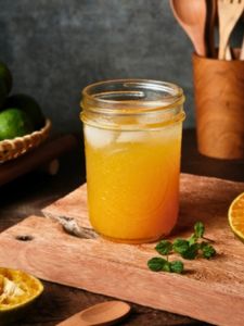 Cocktail sans alcool bella luna avec jus d'orange, ananas et citron vert, dans une mason jar, posée sur une planche à découper en bois.