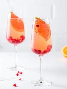 Cocktail Fizz pamplemousse aux fruits rouges sans alcool servi dans une flûte à champagne avec des grains de grenade en garniture et une tranche de pamplemousse