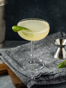 Cocktail gimlet sans bulle avec du gin et du citron servi dans un verre à cocktail avec un zeste de citron