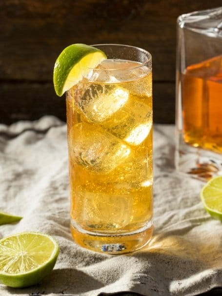 Cocktail Ginger Highball dans un verre long drink avec des glaçons et un quartier de citron vert, à base de whisky, de ginger beer et de jus de citron vert.