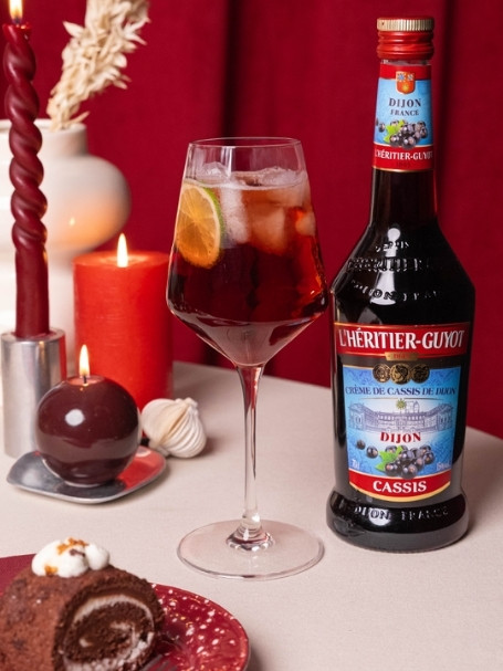 Cocktail Spritz Cassis à la Française par l'Héritier-Guyot, à base de crème de cassis, de crémant et d'eau gazeuse, dans un verre ballon.