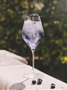 Cocktail Spritz à la violette avec du prosecco et crème de violette servi dans un verre piscine avec des glaçons