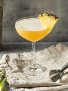 Cocktail Daïquiri Ananas, servi dans un verre à cocktail décoré d'un morceau d'ananas et posé sur un torchon.