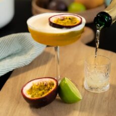 Cocktail Porn Star Martini, servi dans un verre à pied et décoré d'une moitié de fruit de la passion. Le cocktail est accompagné d'un shot de vin pétillant.