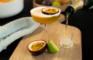 Cocktail Porn Star Martini, servi dans un verre à pied et décoré d'une moitié de fruit de la passion. Le cocktail est accompagné d'un shot de vin pétillant.