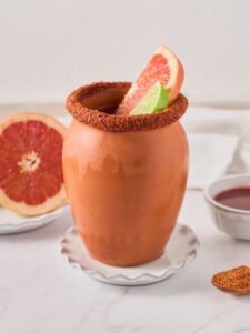 Cocktail Cantarito, une recette à base de tequila, servie dans un pot en argile, givré de tajin et décoré d'une tranche de pamplemousse et de citron vert.