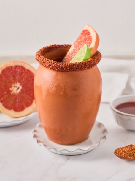 Cocktail Cantarito, une recette à base de tequila, servie dans un pot en argile, givré de tajin et décoré d'une tranche de pamplemousse et de citron vert.