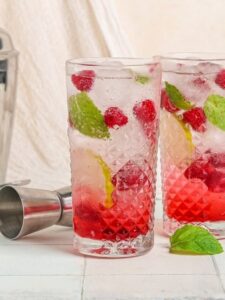 Cocktail Virgin Mojito Framboise, dans un verre à mojito, à base de rhum désalcoolisé, de sirop de framboise, de framboises, de feuilles de menthe, de citron vert et d'eau gazeuse, avec des glaçons.