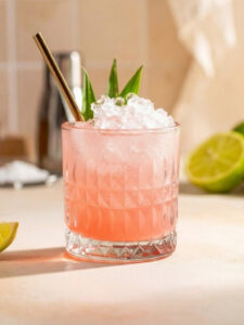 Cocktail Doctor Funk, dans un verre old fahsioned avec de la glace pilée, à base de rhum ambré, d'absinthe, de sirop de grenadine, d'eau gazeuse, de jus de citron jaune et vert, avec des feuilles de palmier en décoration et une paille.